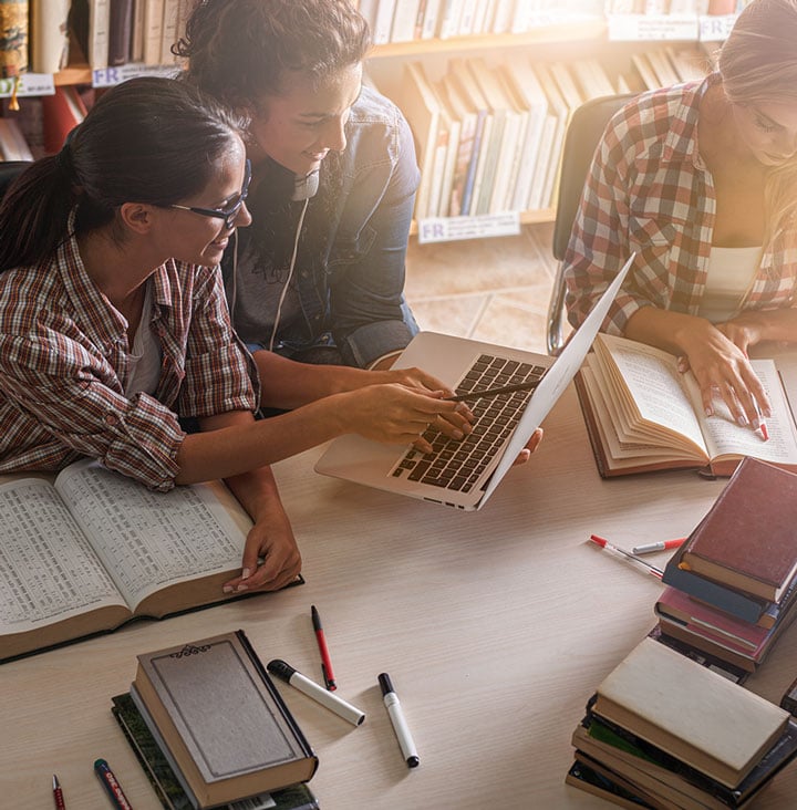 students comparing notes on laptop at library